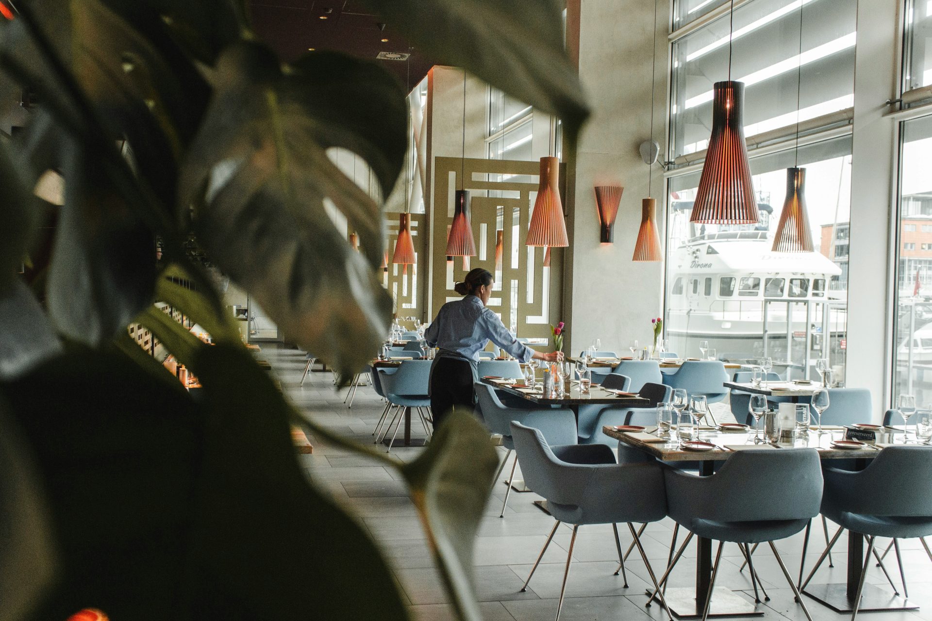Une femme devant une table et des chaises de salle à manger brunes, à l'intérieur d'un bâtiment.